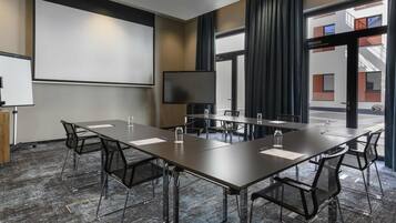 Un salón de conferencias con una larga mesa, sillas, una pantalla de proyector y un televisor.