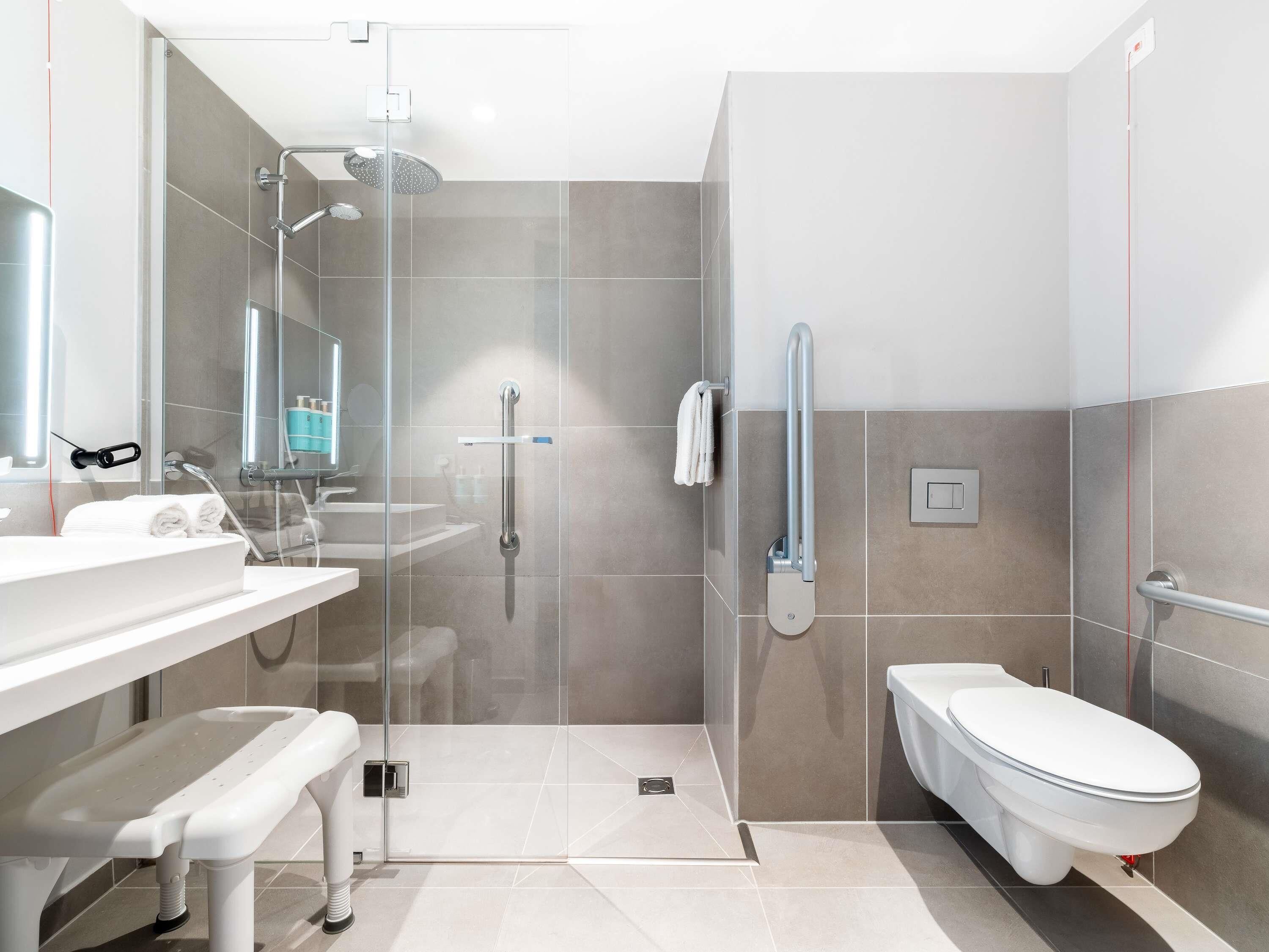 A modern bathroom with a glass shower enclosure, a toilet, and a sink with a bench.
