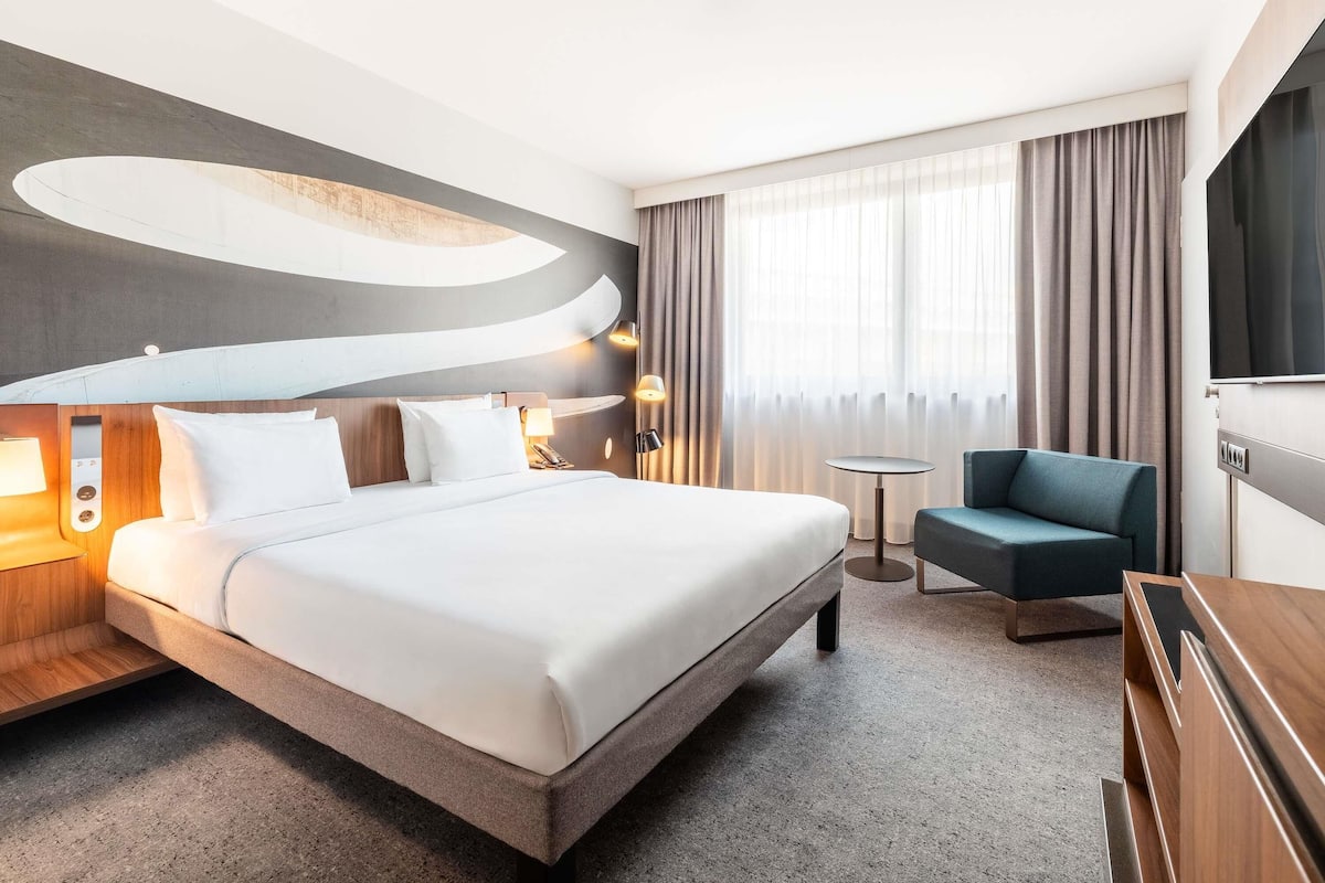Una habitación de hotel moderna con una cama grande, un escritorio pequeño, una silla y un televisor.