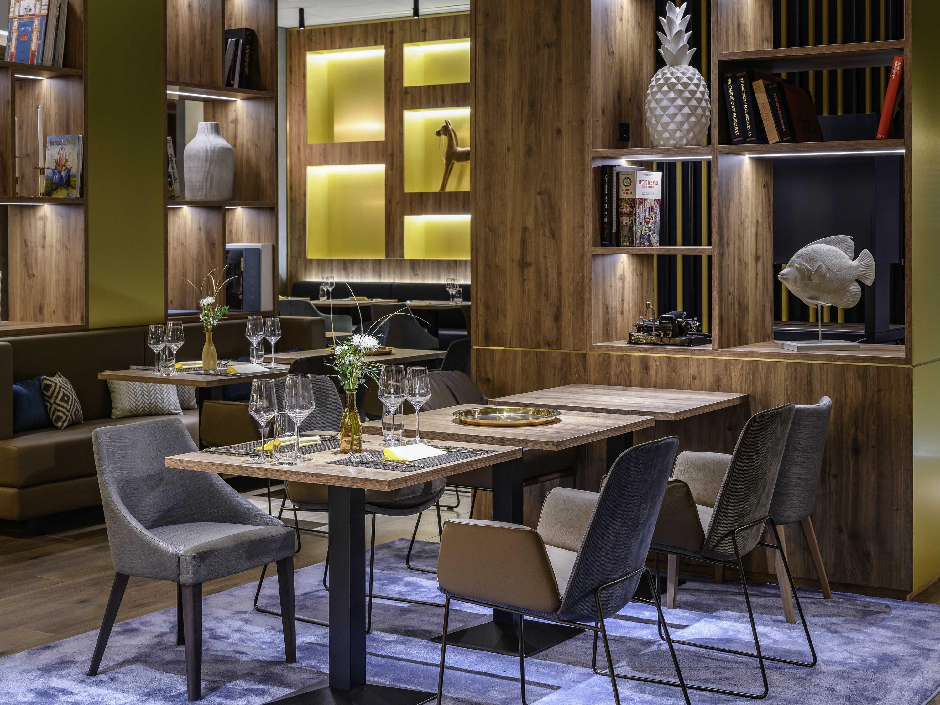 A modern dining area with wooden furniture, a central table with chairs, and a bookshelf with books and decorative items.