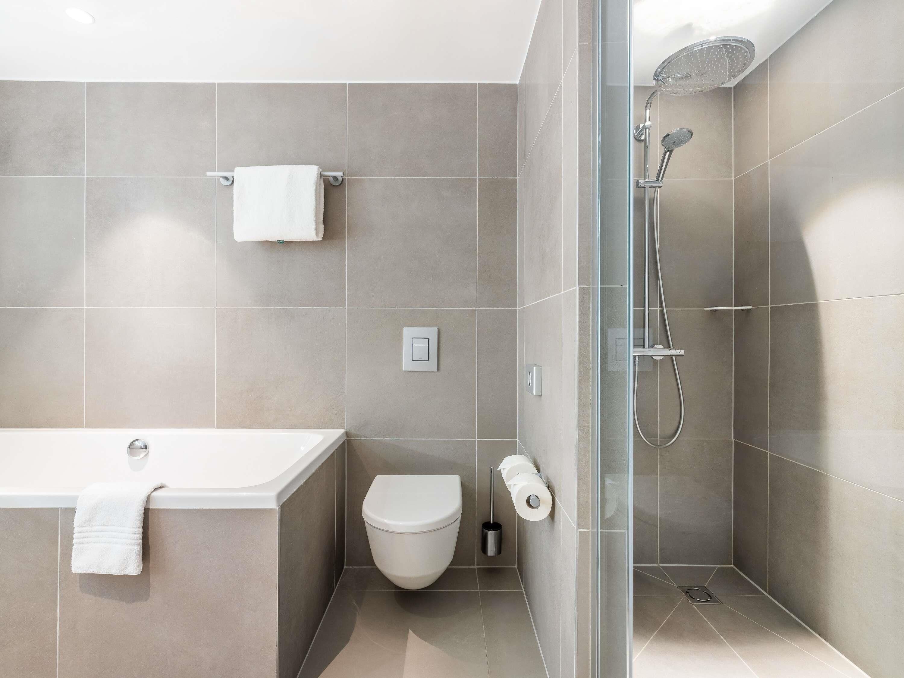 Egy modern fürőszoba, amelyben kád, WC és üvegfalakkal elválasztott zuhanyzó található.