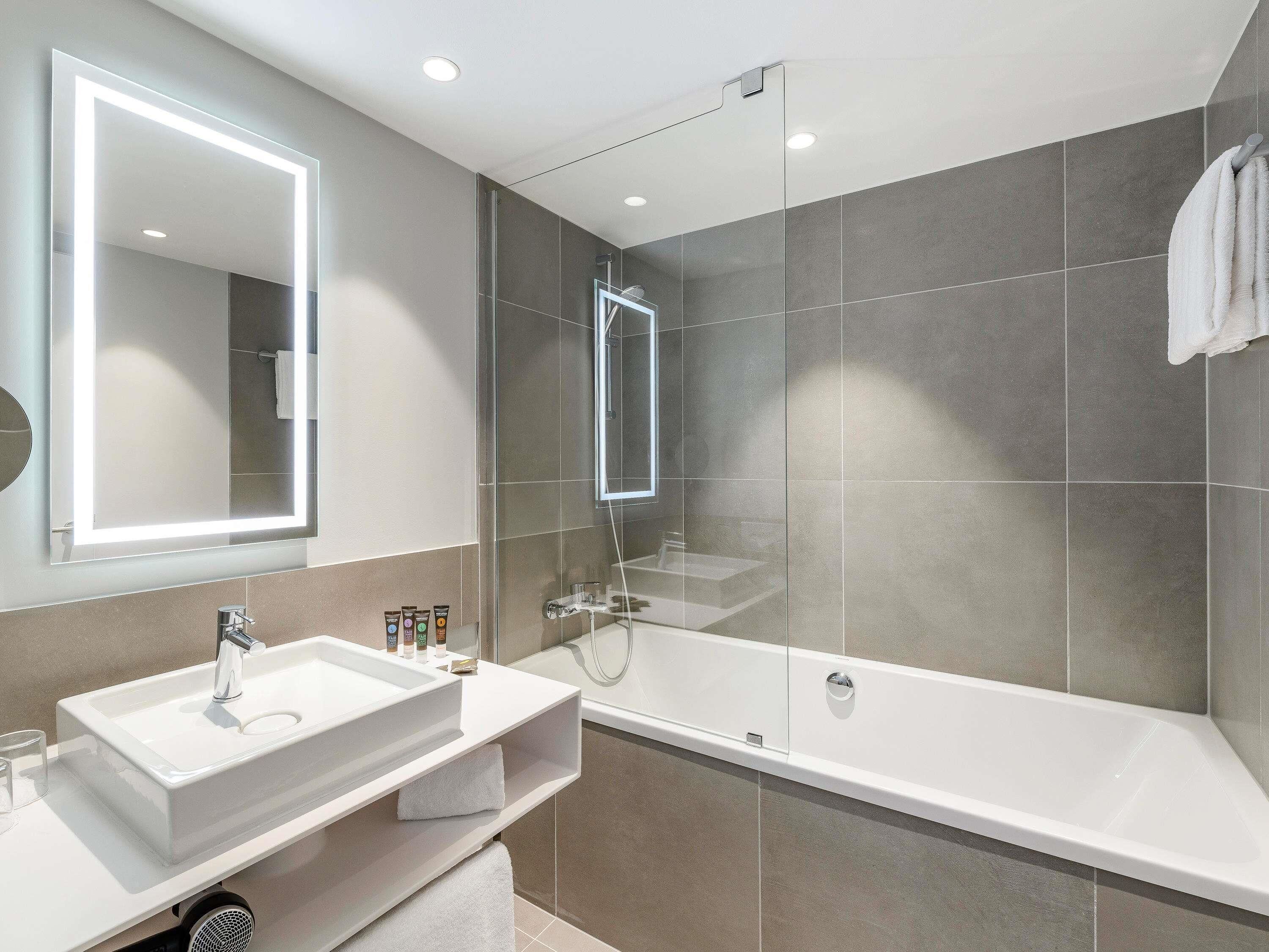 A modern bathroom with a large mirror, a bathtub, and a vanity with a sink.
