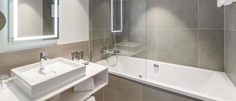 A modern bathroom with a large mirror, a bathtub, and a vanity with a sink.