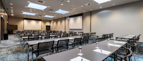 Un salón de conferencias con mesas, sillas, una pantalla de proyector y piso alfombrado.