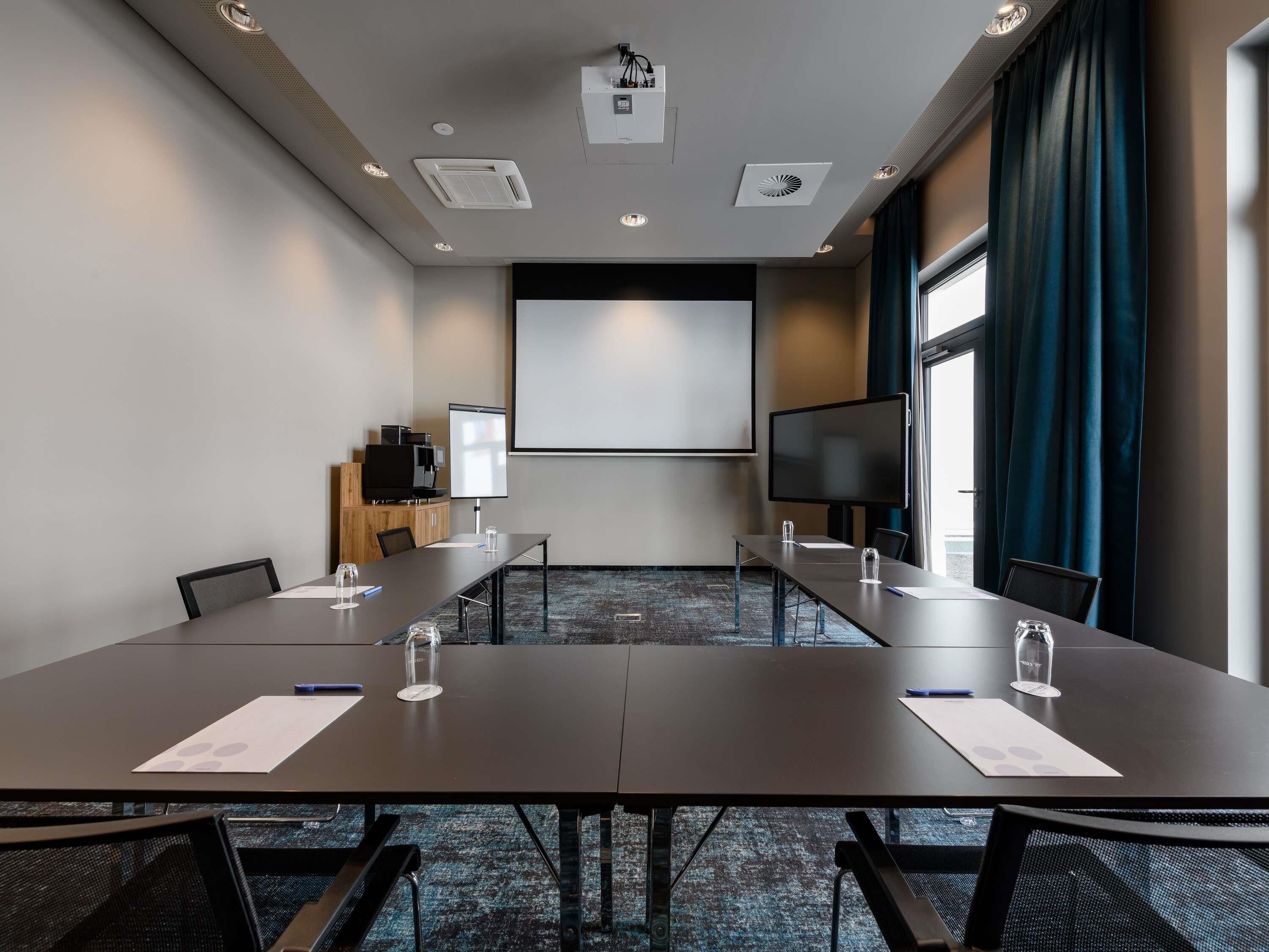Une salle de conférence équipée d’une grande table, de chaises, d’un écran de projection et d’un téléviseur.