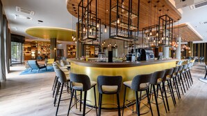 Un área de bar moderna con una barra central, varios taburetes, lámparas colgantes y techo de madera.