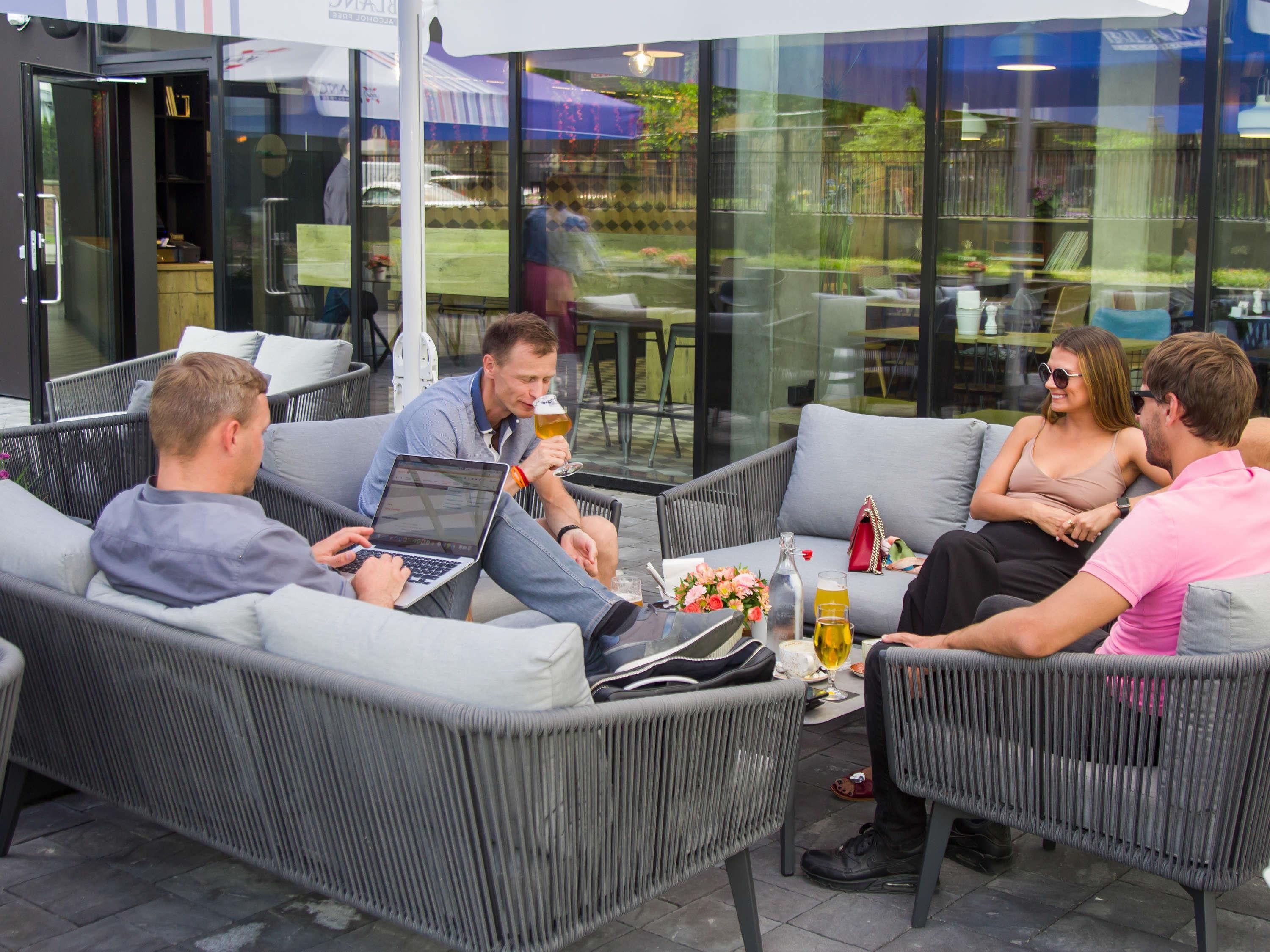 Un grupo de personas sentadas en muebles de mimbre al aire libre, con una mesa de vidrio, una computadora portátil y bebidas.