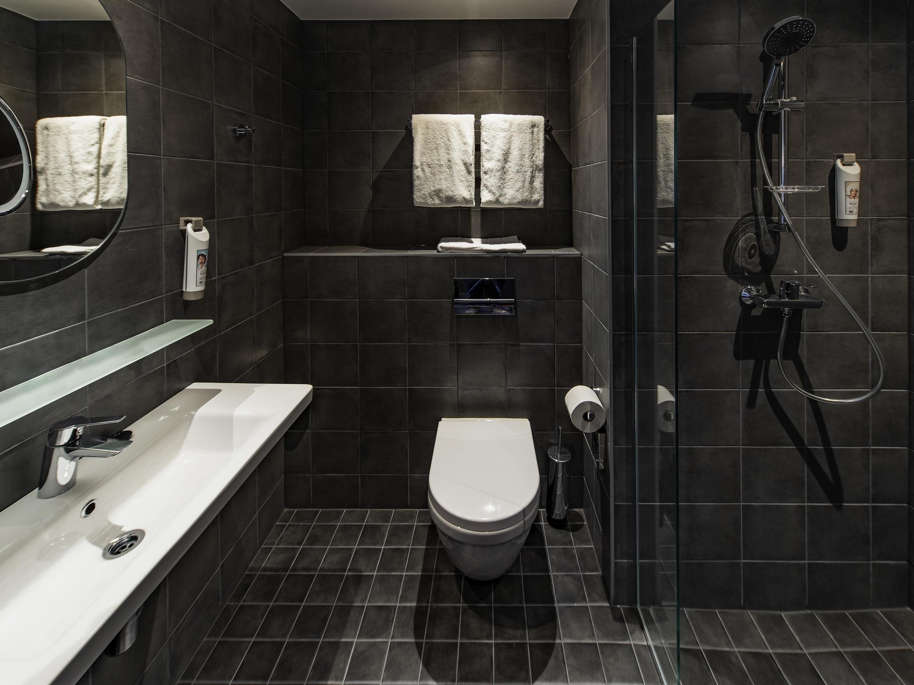 A modern bathroom with a white toilet, a glass shower enclosure, and a large mirror.