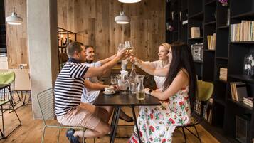 A group of people toasting at a wooden table in a room with bookshelves and pendant lighting.