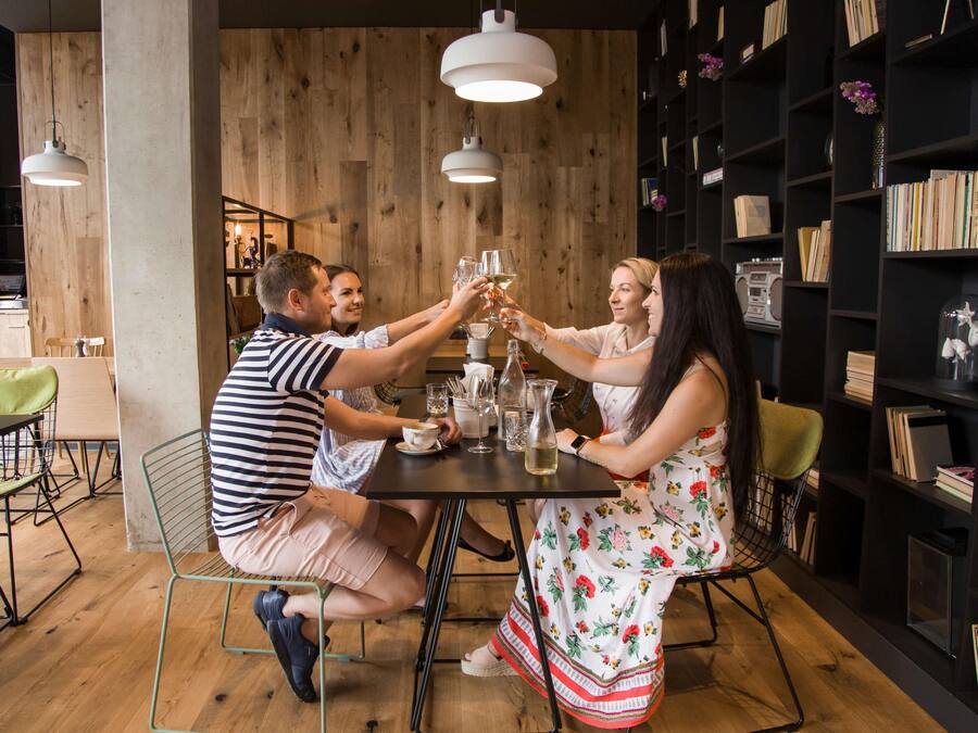 A group of people toasting at a wooden table in a room with bookshelves and pendant lighting.