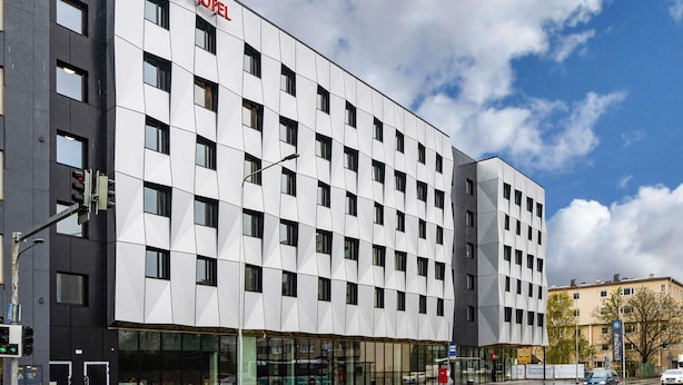 Un bâtiment d’hôtel moderne, caractérisé par une façade à motifs géométriques de fenêtres et une enseigne « ibis hotel » bien visible.
