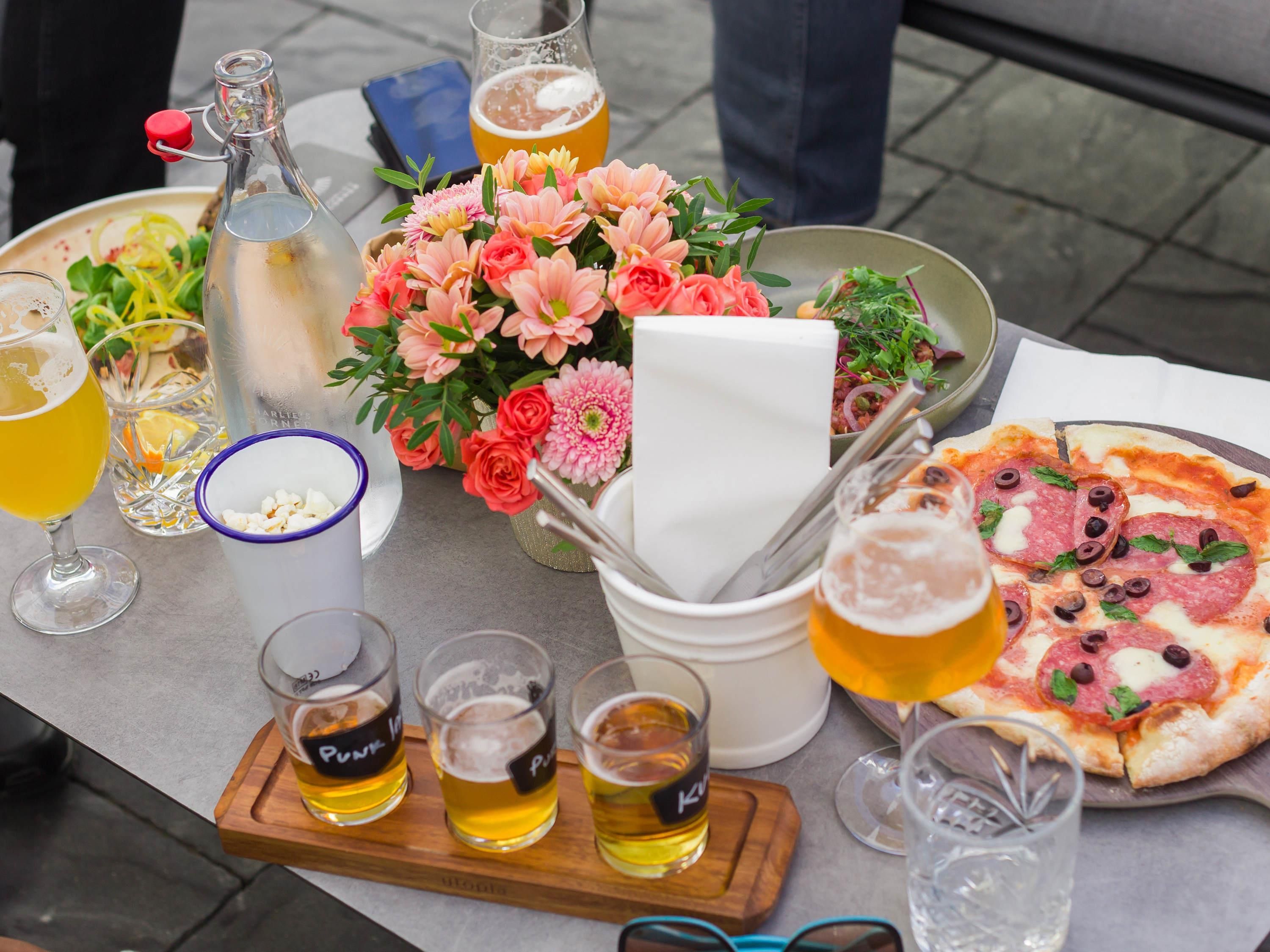 A table with a pizza, drinks, a bottle, and a bouquet of flowers.