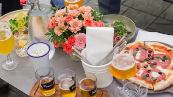 Een tafel met pizza, drankjes, een fles en een boeket bloemen.