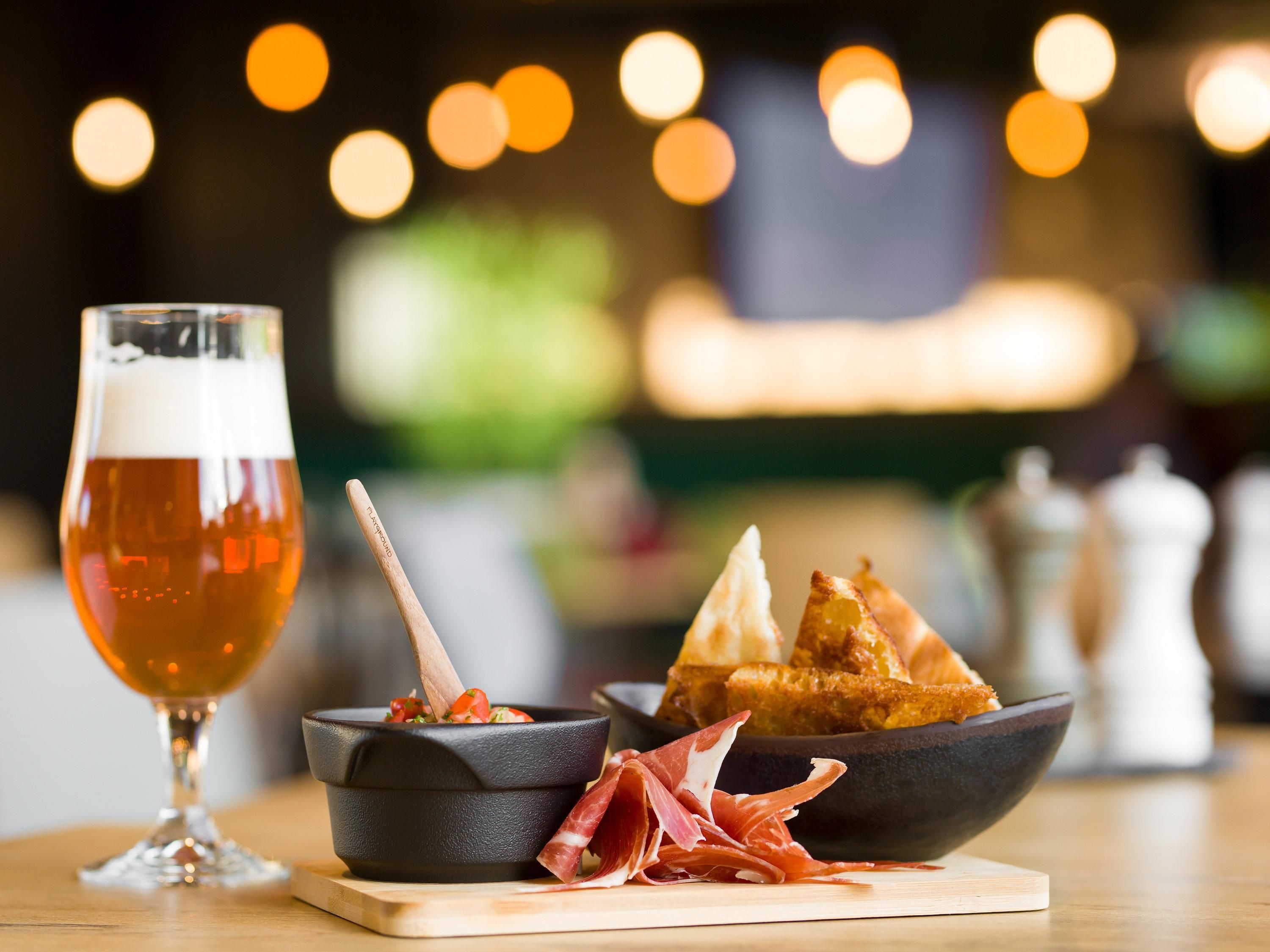 Une table avec un verre de bière, un bol de nourriture et une assiette de pain.