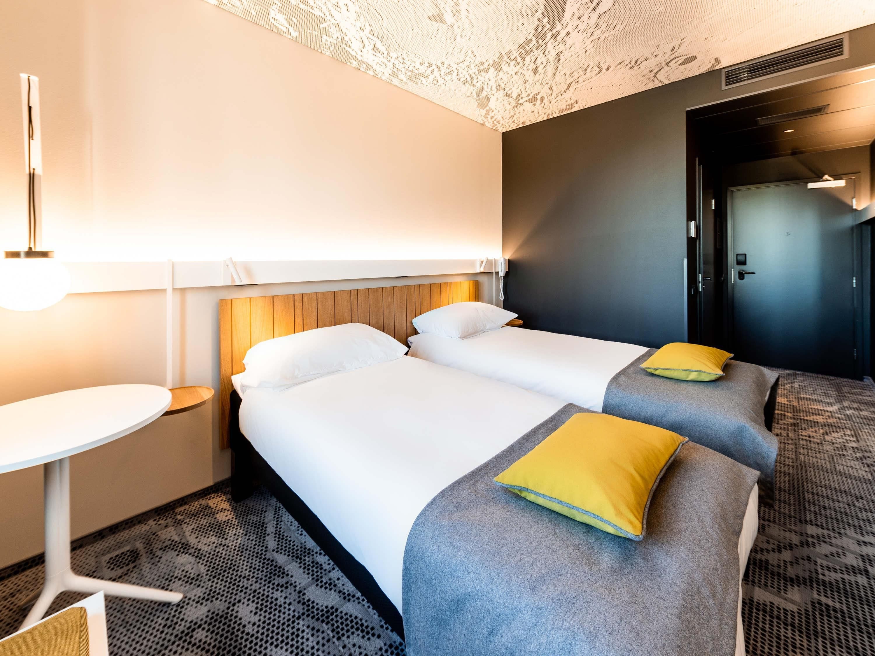 A hotel room with two beds, a small table, and a door.