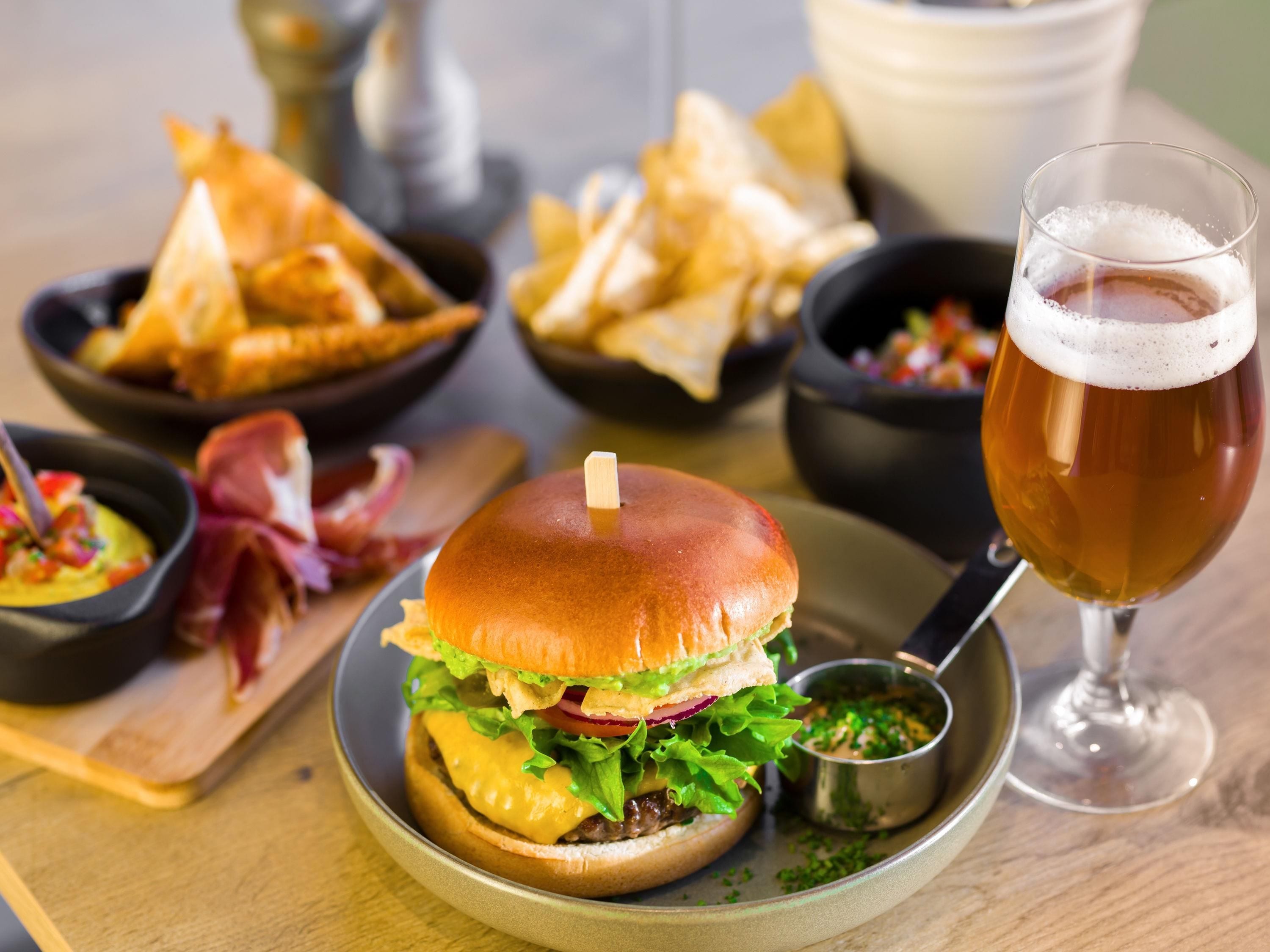 A burger with a side of chips and a glass of beer on a wooden table.