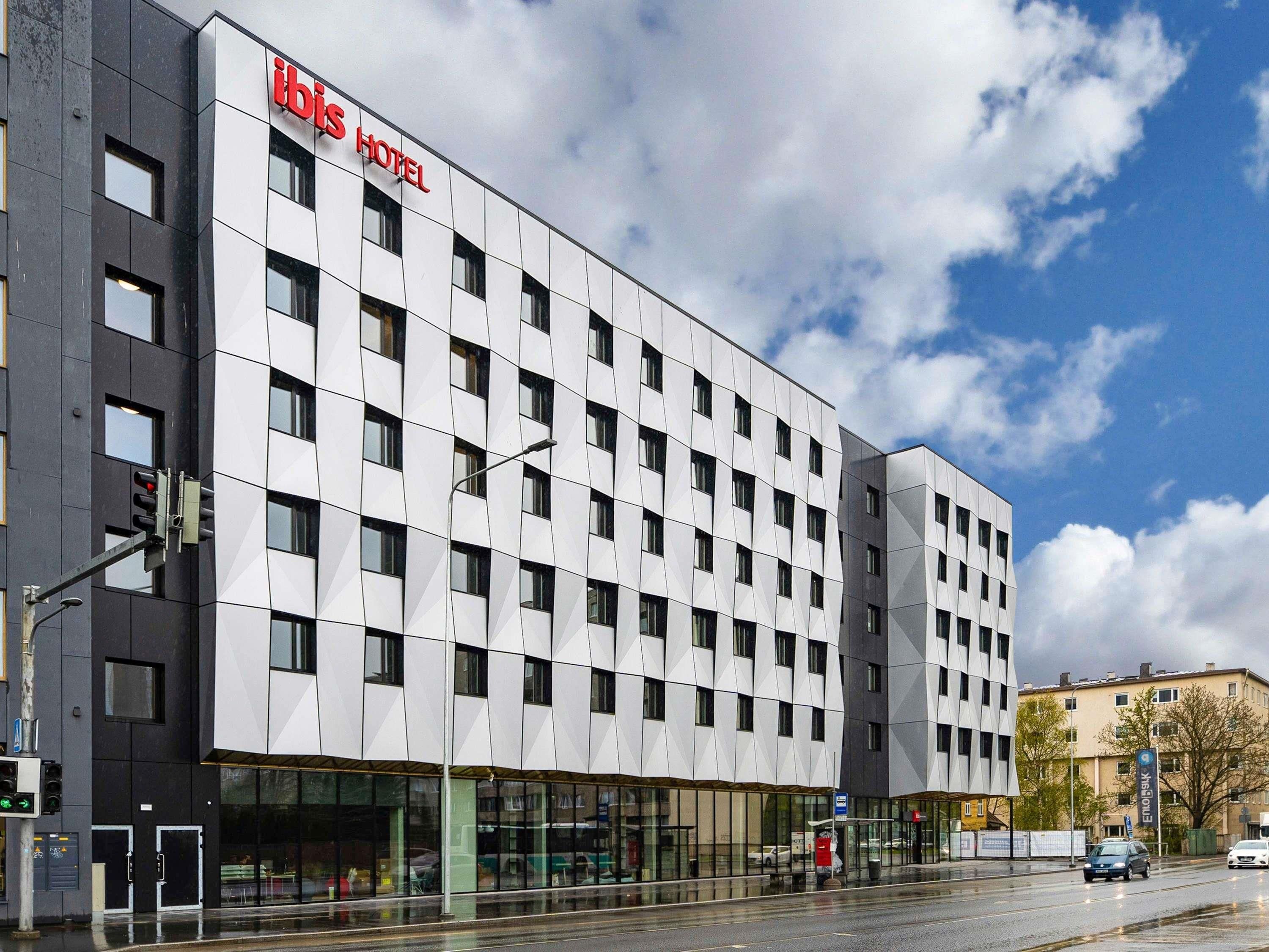 Um hotel moderno com fachada em grade de janelas e um letreiro grande com a inscrição 'ibis hotel'.