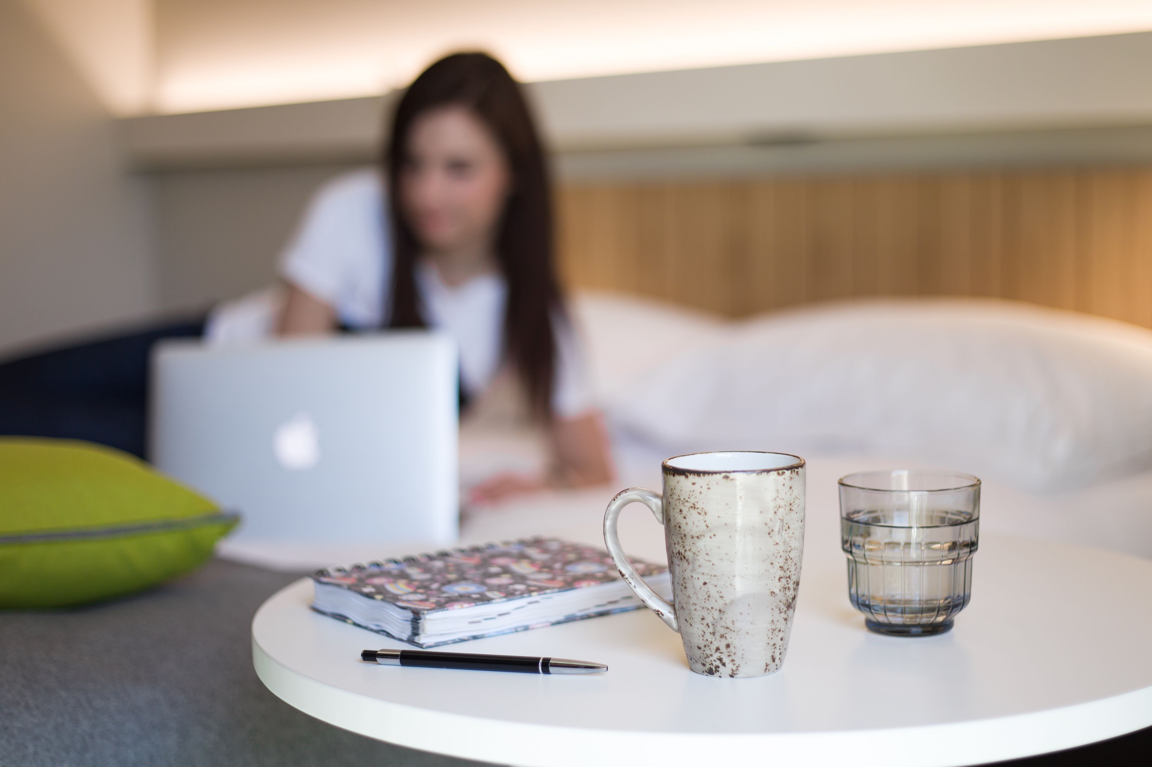 A round white table with a notebook, a pen, a ceramic mug, and a glass of water.