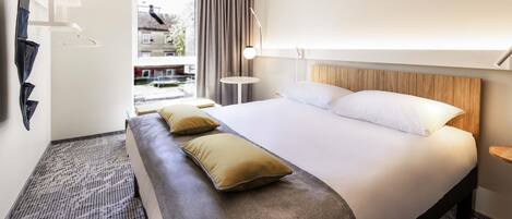 Quarto de hotel com uma cama grande, um banco, uma mesinha e vista para o exterior.