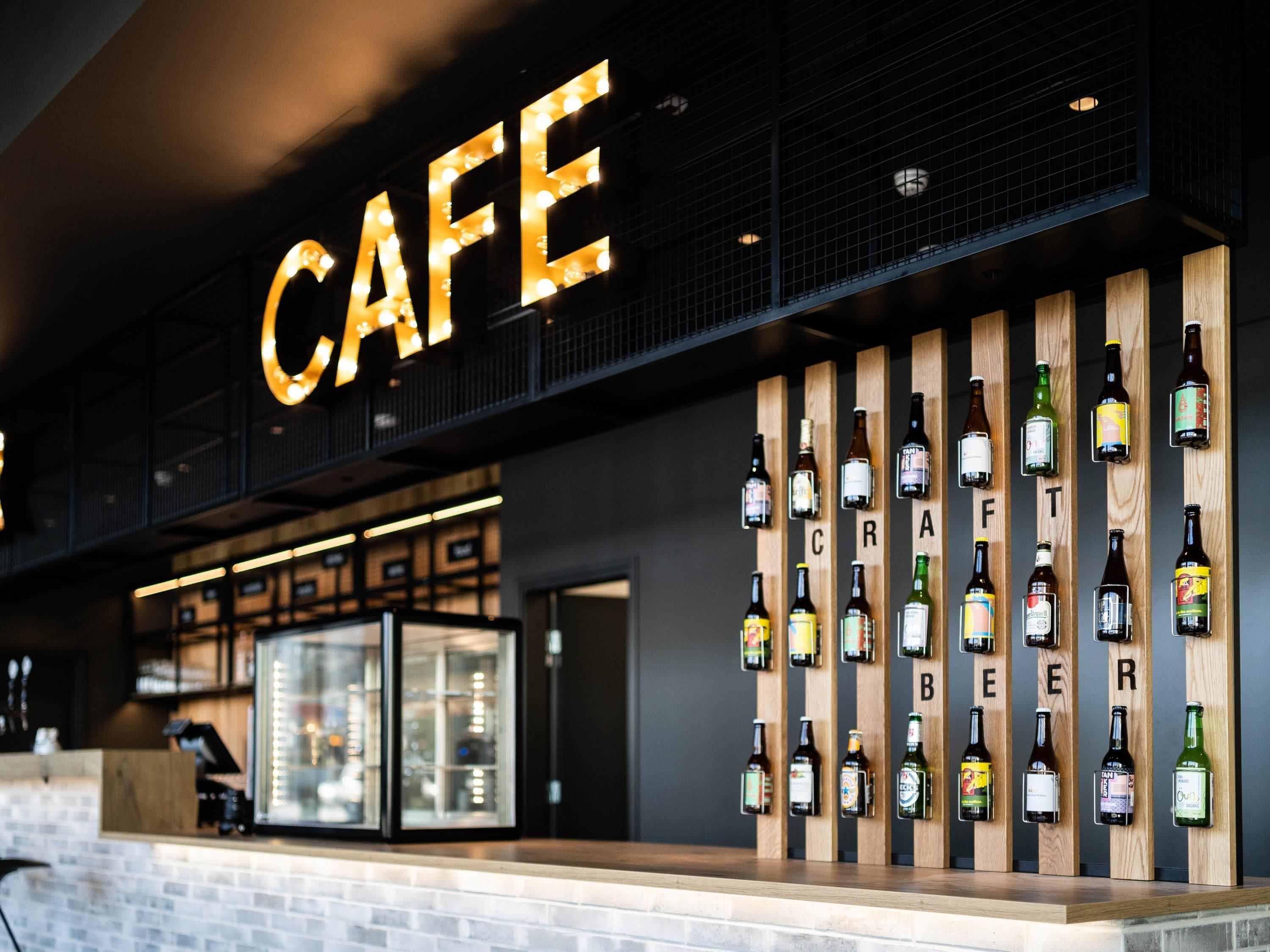 Een café met een opvallend bord waarop 'CAFE' staat, en een muur met verschillende bierflesjes.