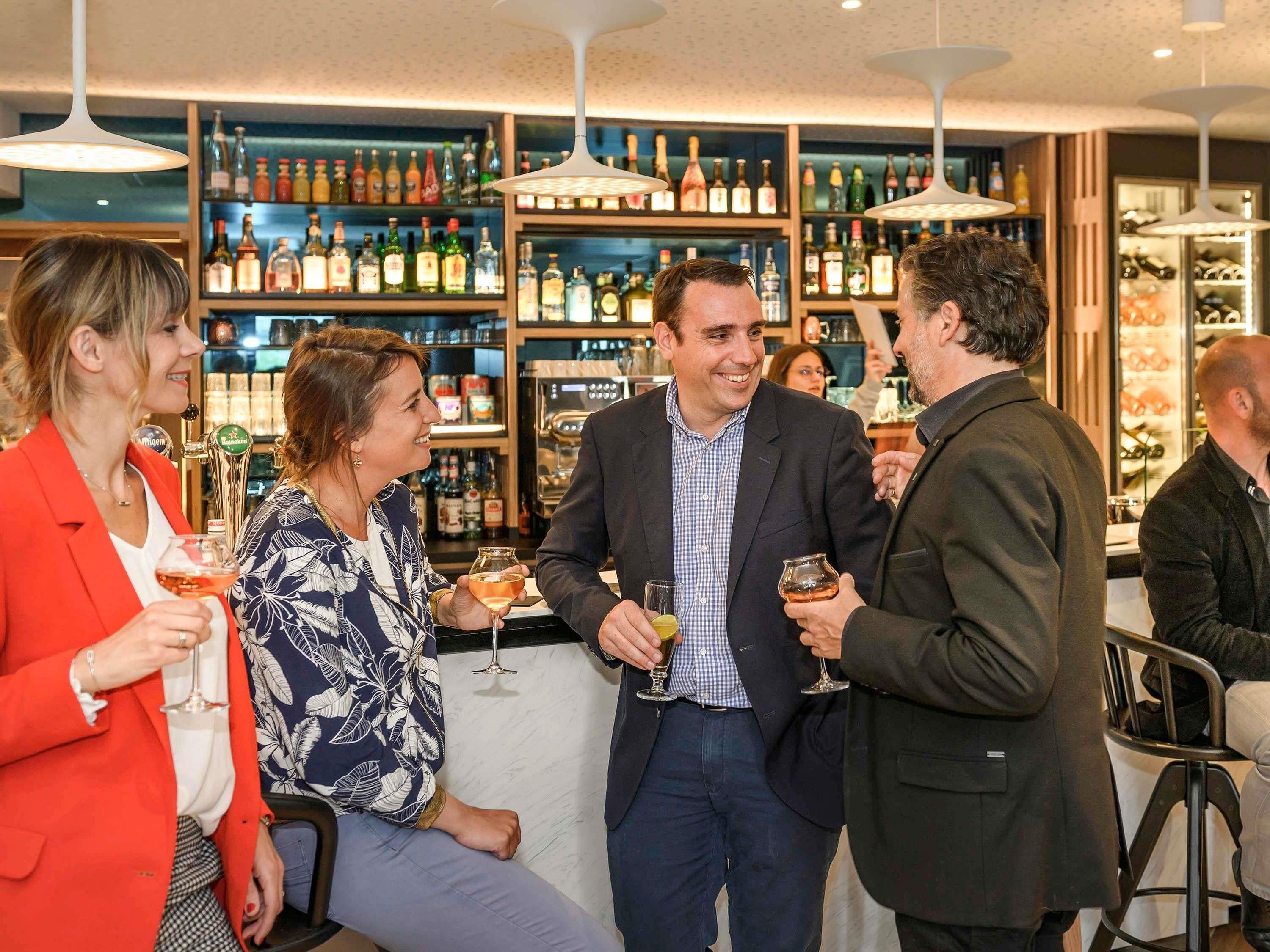 A bar area with multiple people conversing, shelves stocked with bottles, and a modern ceiling design.
