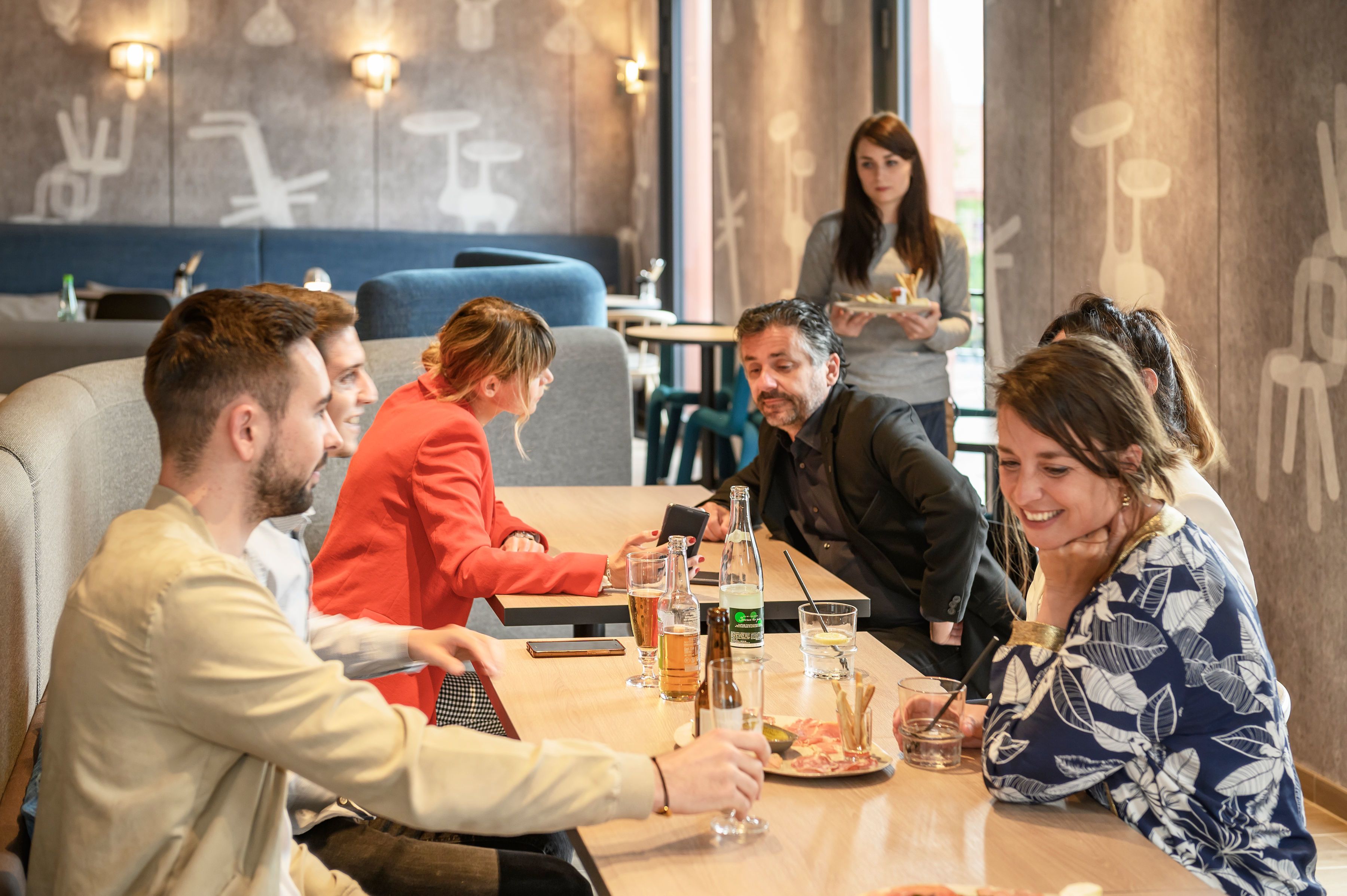 A group of people dining at a restaurant with a modern interior, including a blue cushioned booth and a wall with abstract designs.