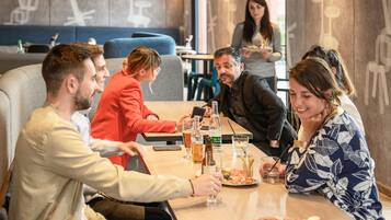 A group of people dining at a restaurant with a modern interior, including a blue cushioned booth and a wall with abstract designs.