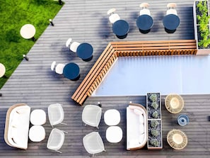 A poolside area with multiple seating options, including round tables and chairs, and a wooden deck. - Novotel Saint-Étienne Centre Gare Châteaucreux (Saint-Etienne)