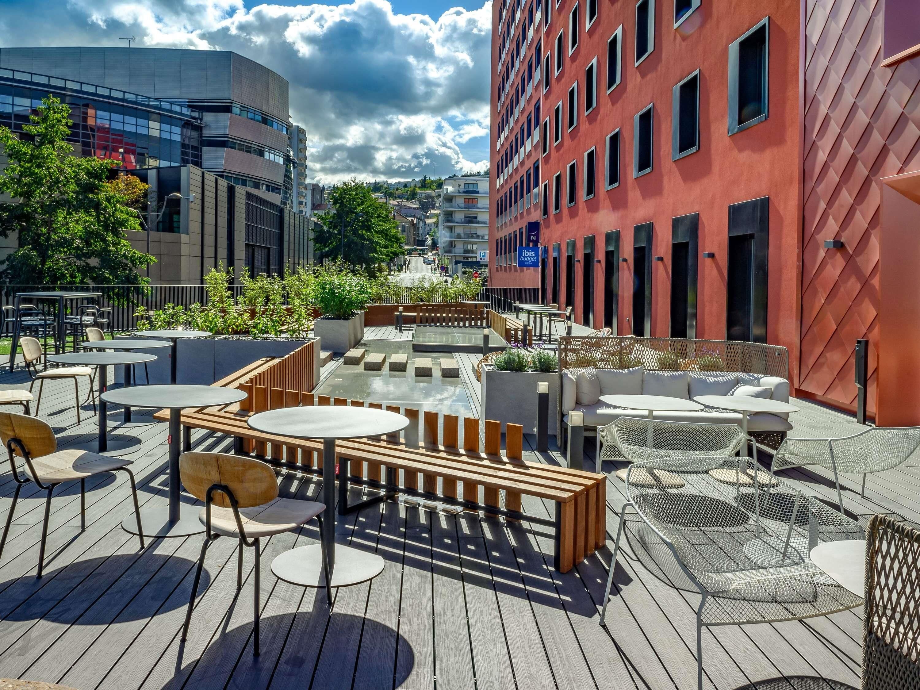 Un espace extérieur aménagé avec des tables et des chaises, entouré d’une terrasse en bois et de verdure.
