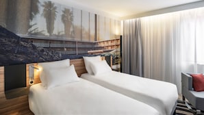 A hotel room with two beds, a large painting on the wall, a wooden headboard, and a view of a balcony. - Novotel Saint-Étienne Centre Gare Châteaucreux (Saint-Etienne)