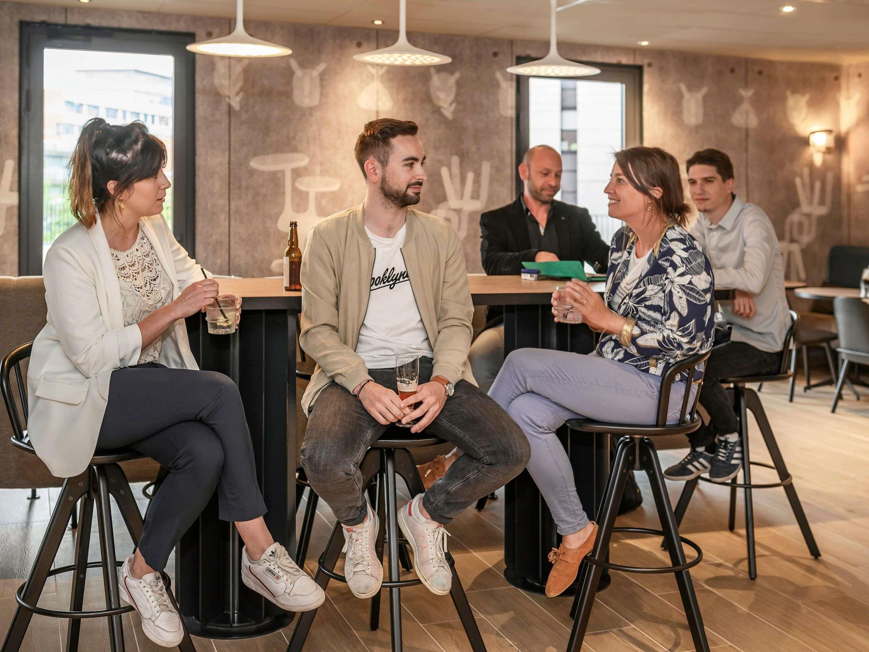 Een groep mensen zit aan een bar met krukken en voert een gesprek.