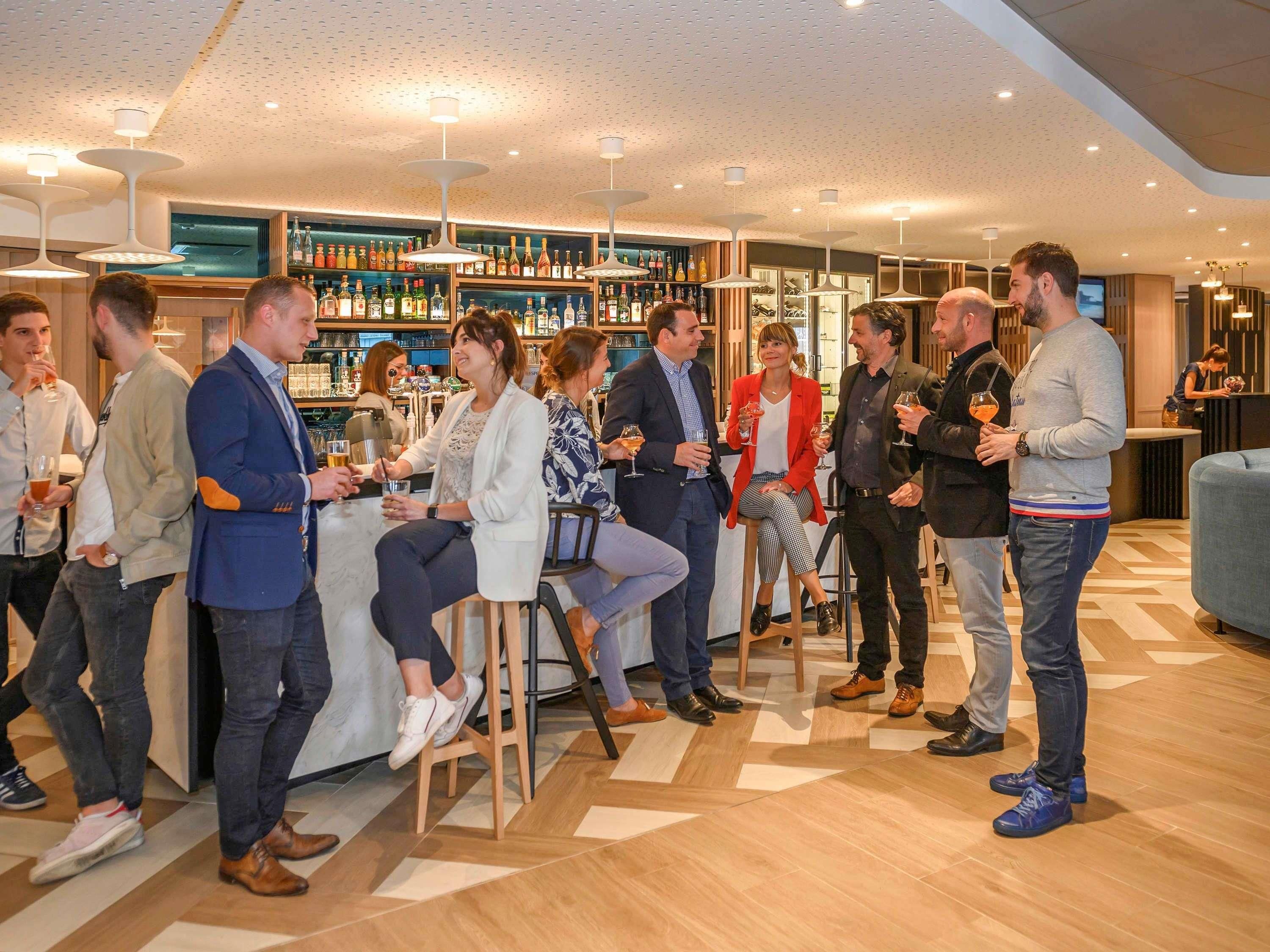 Un grupo de personas en un bar moderno con mostrador y estantes llenos de botellas.