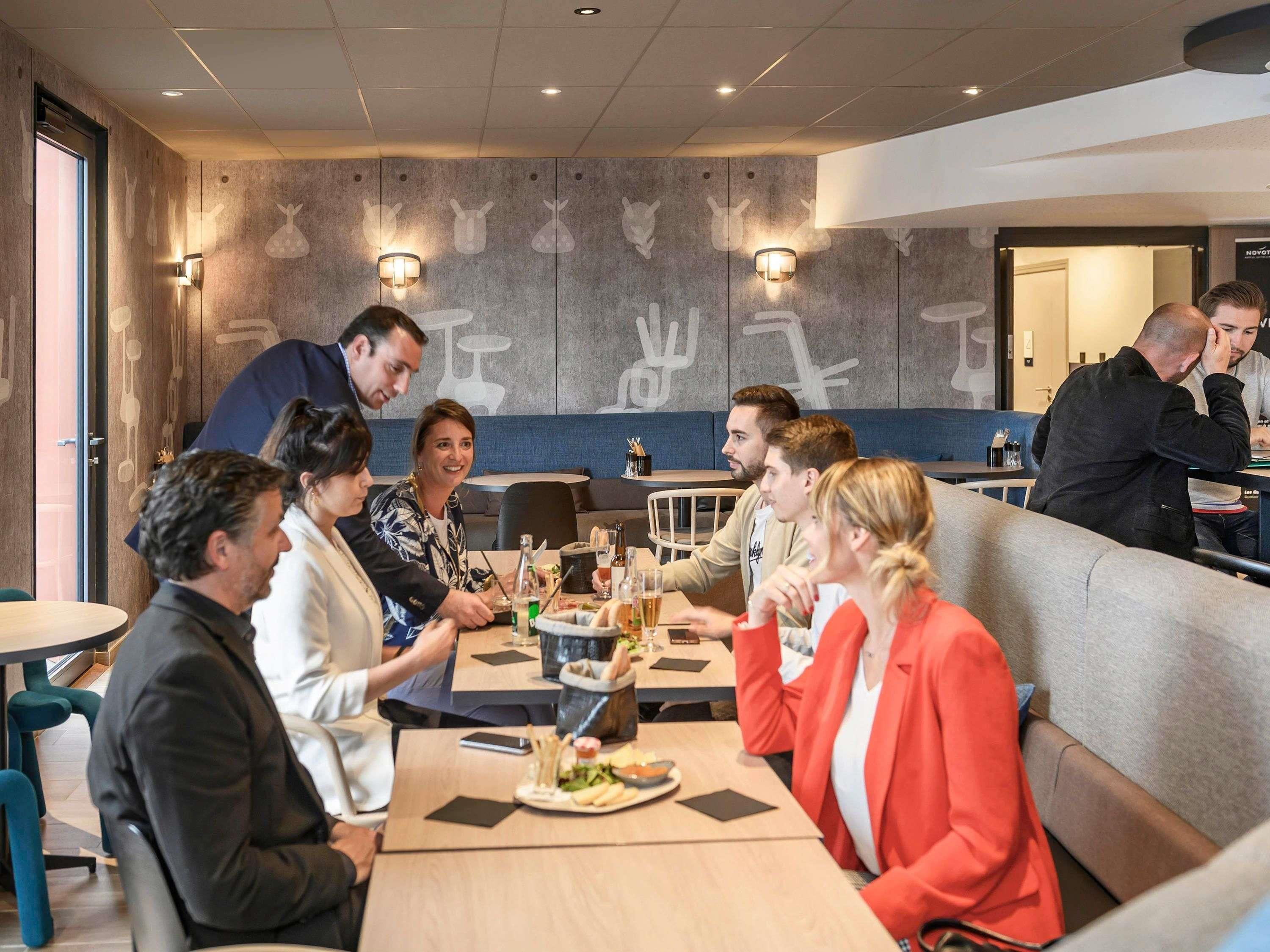 A group of people dining in a restaurant with a modern interior, including a high ceiling and wall-mounted lighting.