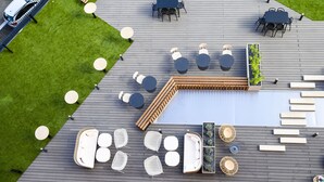 An outdoor deck with multiple seating areas, including round tables and benches, arranged around a central pool. - Novotel Saint-Étienne Centre Gare Châteaucreux (Saint-Etienne)
