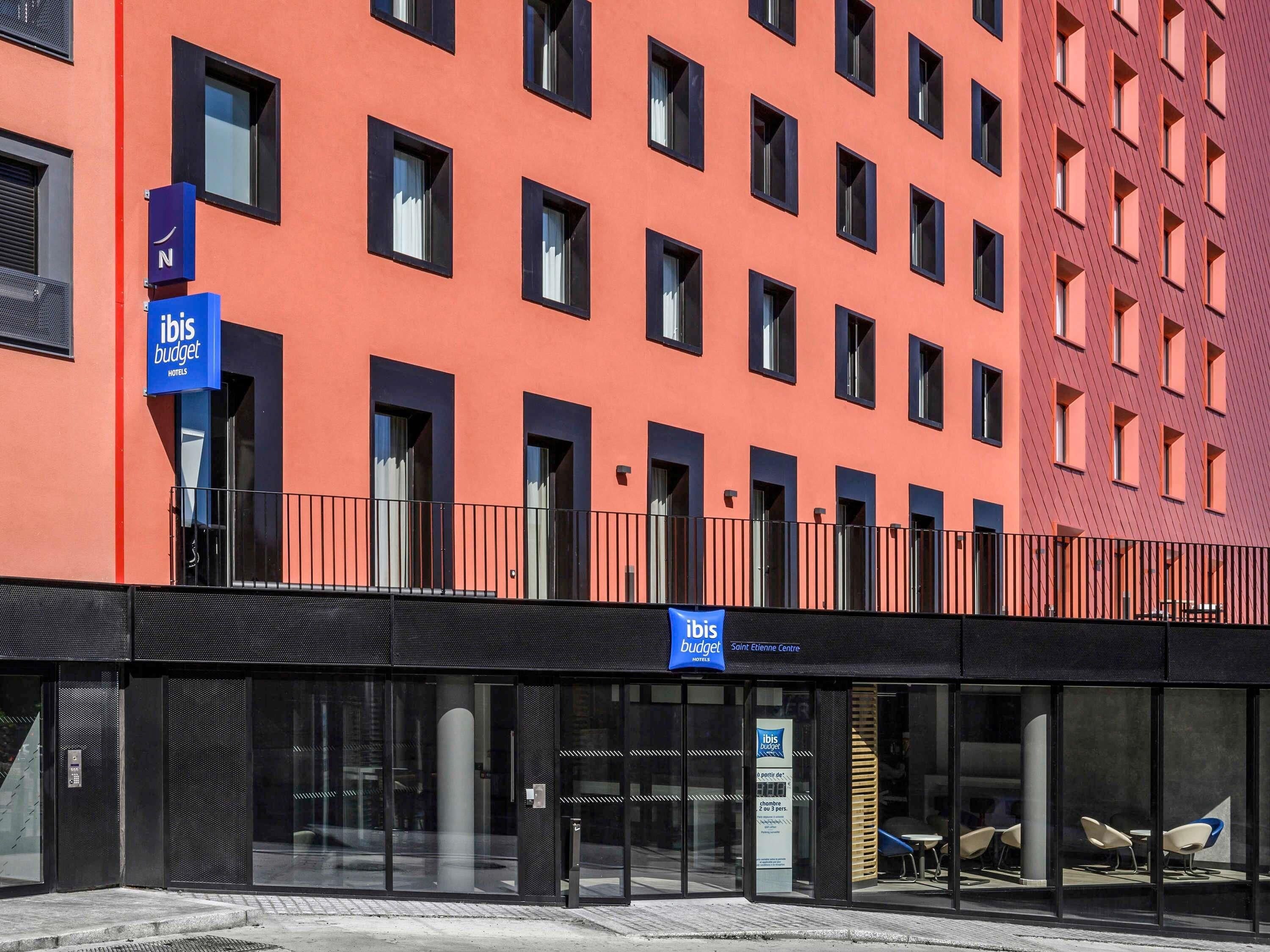 A modern building with a red facade, multiple windows, and a sign for ibis budget hotels.