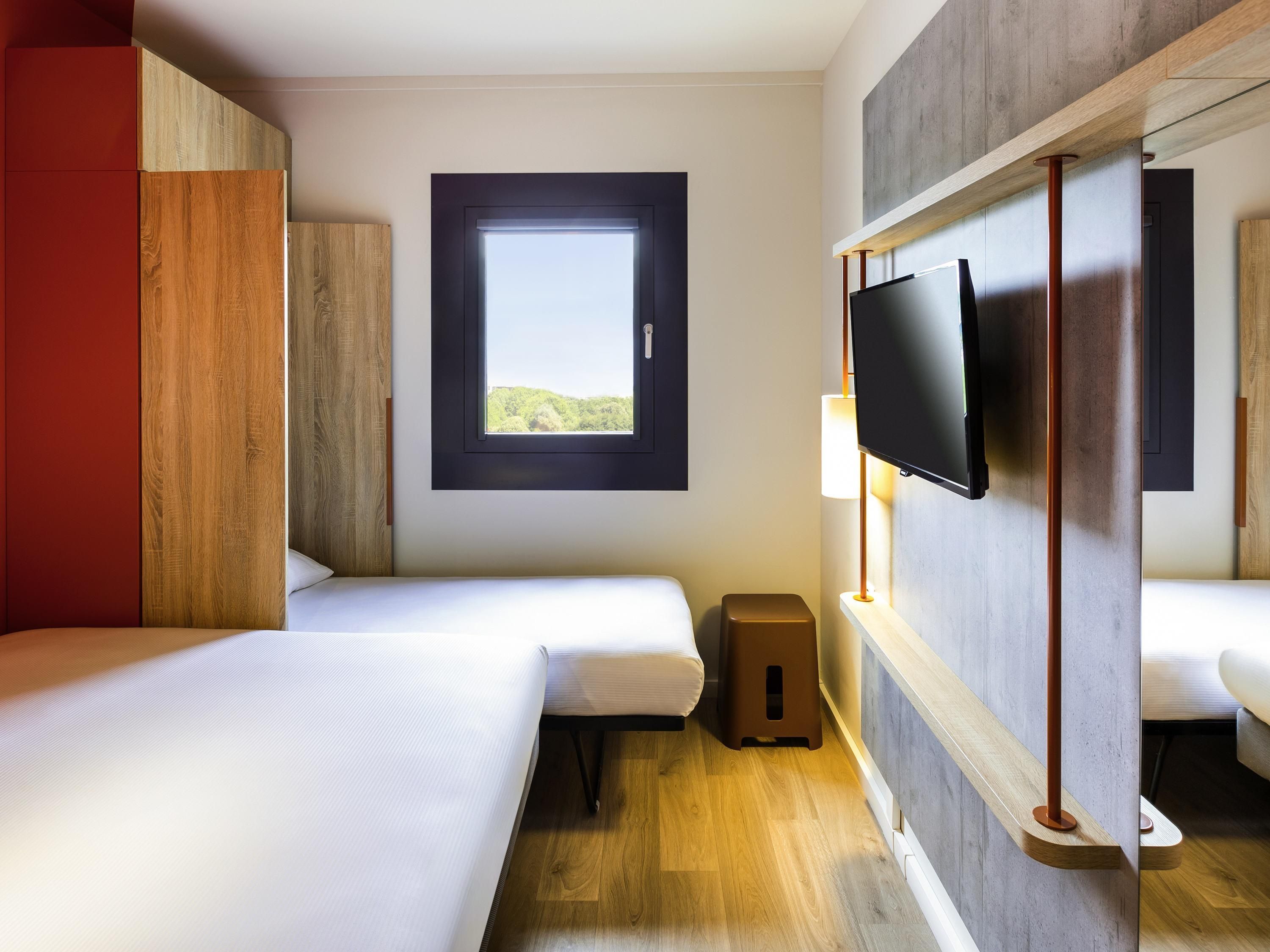 A hotel room with two beds, a TV, a window, and a wooden floor.