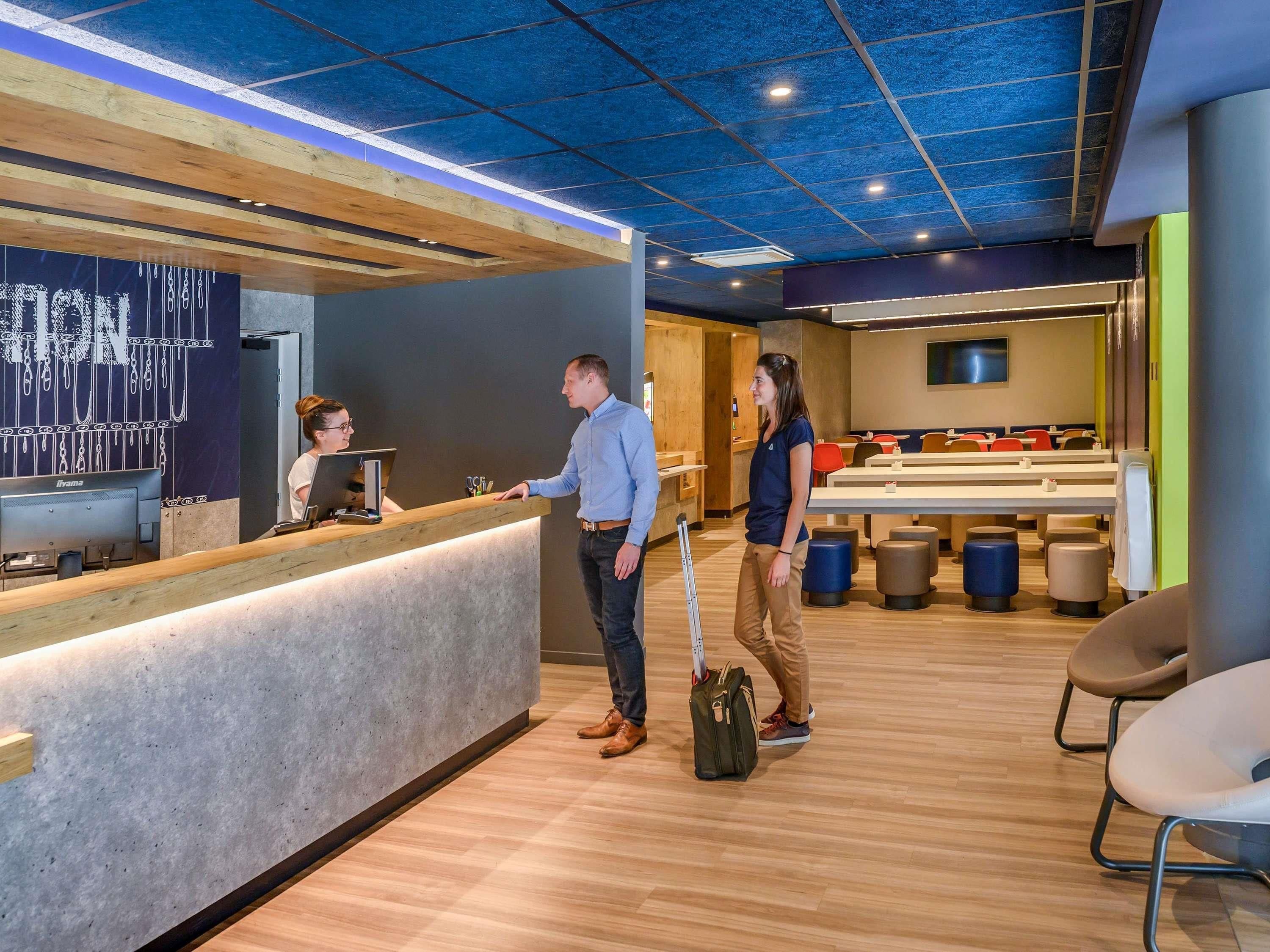A reception area with a wooden counter, a computer, and a seating area with tables and chairs.