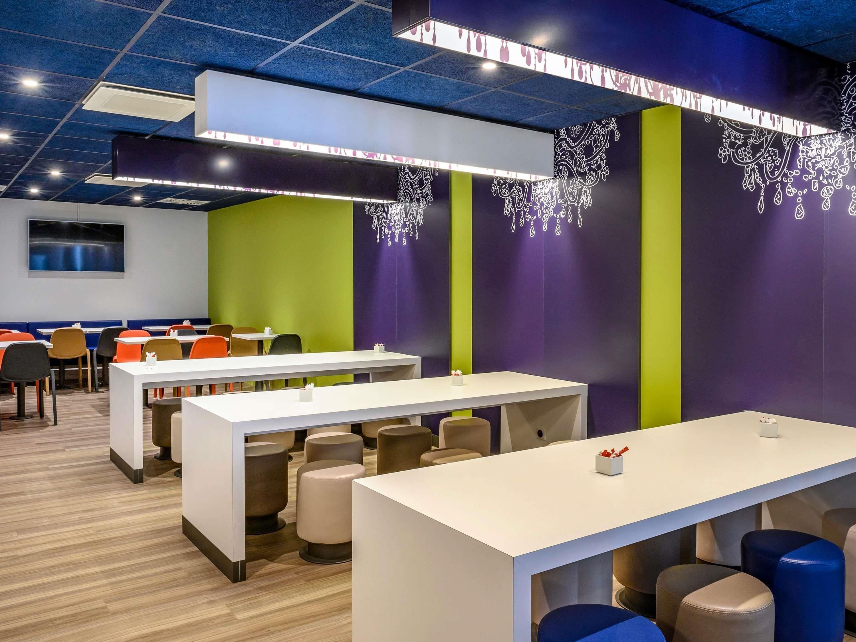Un espace repas moderne avec des tables et des chaises hautes, un téléviseur à écran plat et des motifs décoratifs sur les murs.