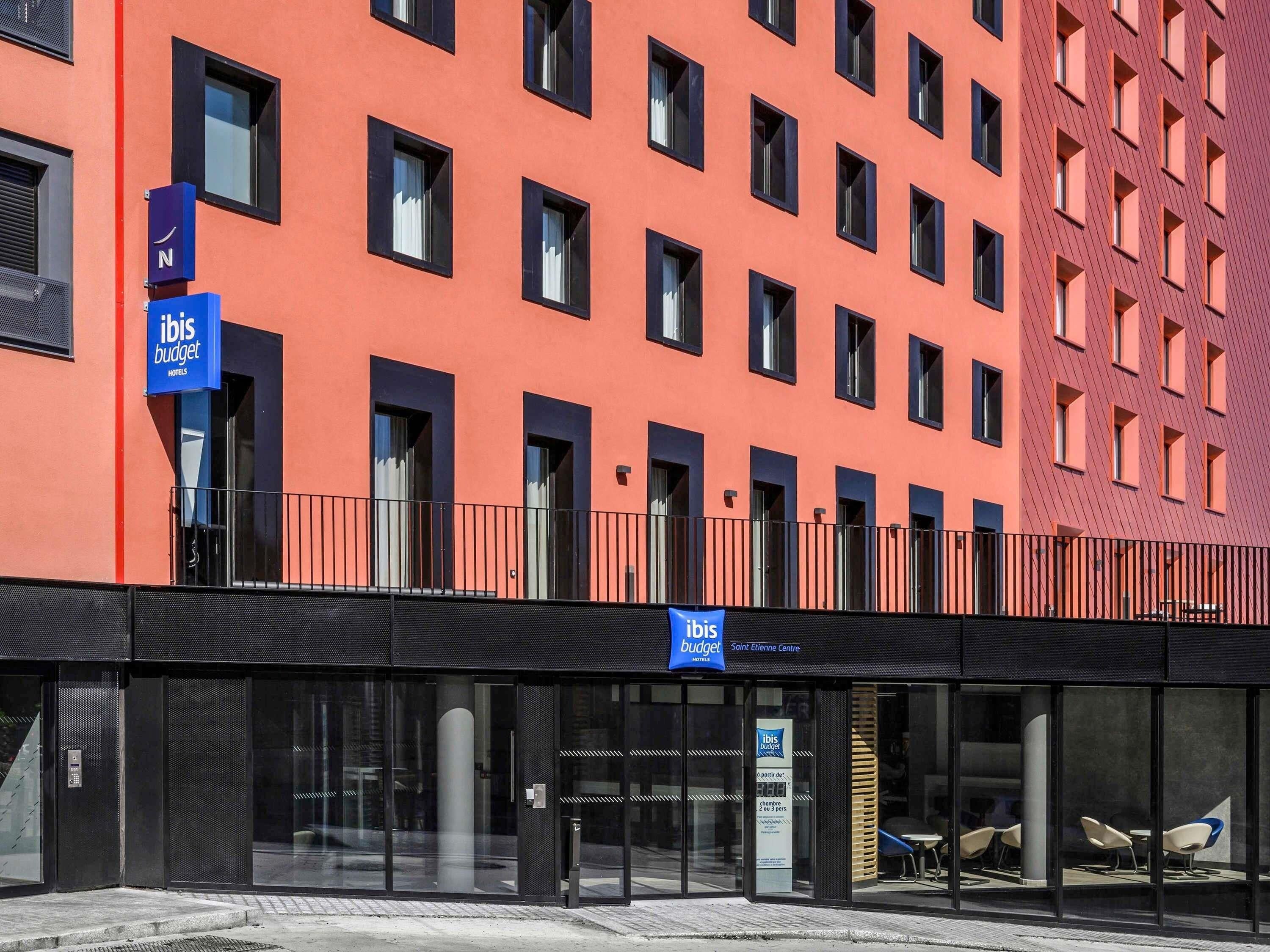 Een modern hotelgebouw met een opvallende oranje kleur, veel ramen en een duidelijke ingang met een glazen deur.