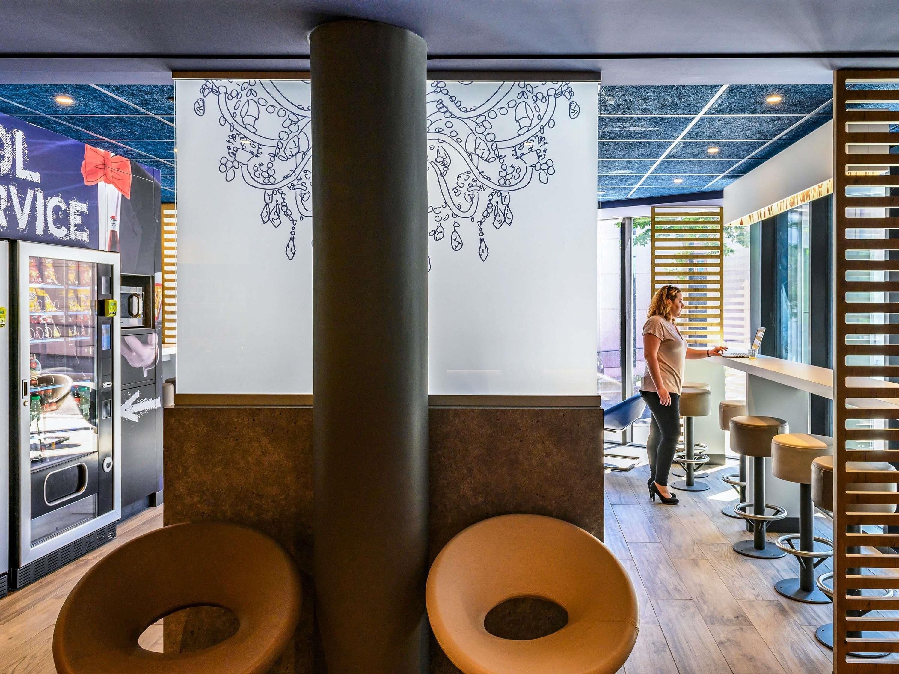 Ein modernes Interieur mit einem Getränkeautomaten, einer großen Wanddekoration und einer Sitzgelegenheit mit Hocker.
