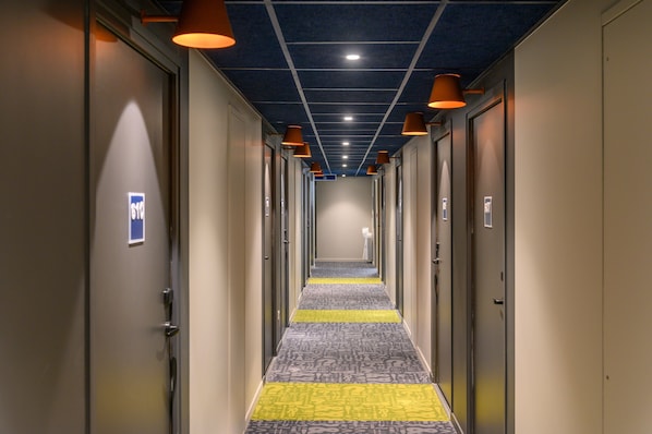 A hotel hallway with doors on both sides, a patterned carpet, and overhead lighting. - Ibis Budget Saint-Etienne Centre Gare Châteaucreux (Saint-Etienne)