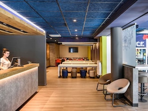 A modern restaurant interior with a wooden reception desk, seating area, and a bar.