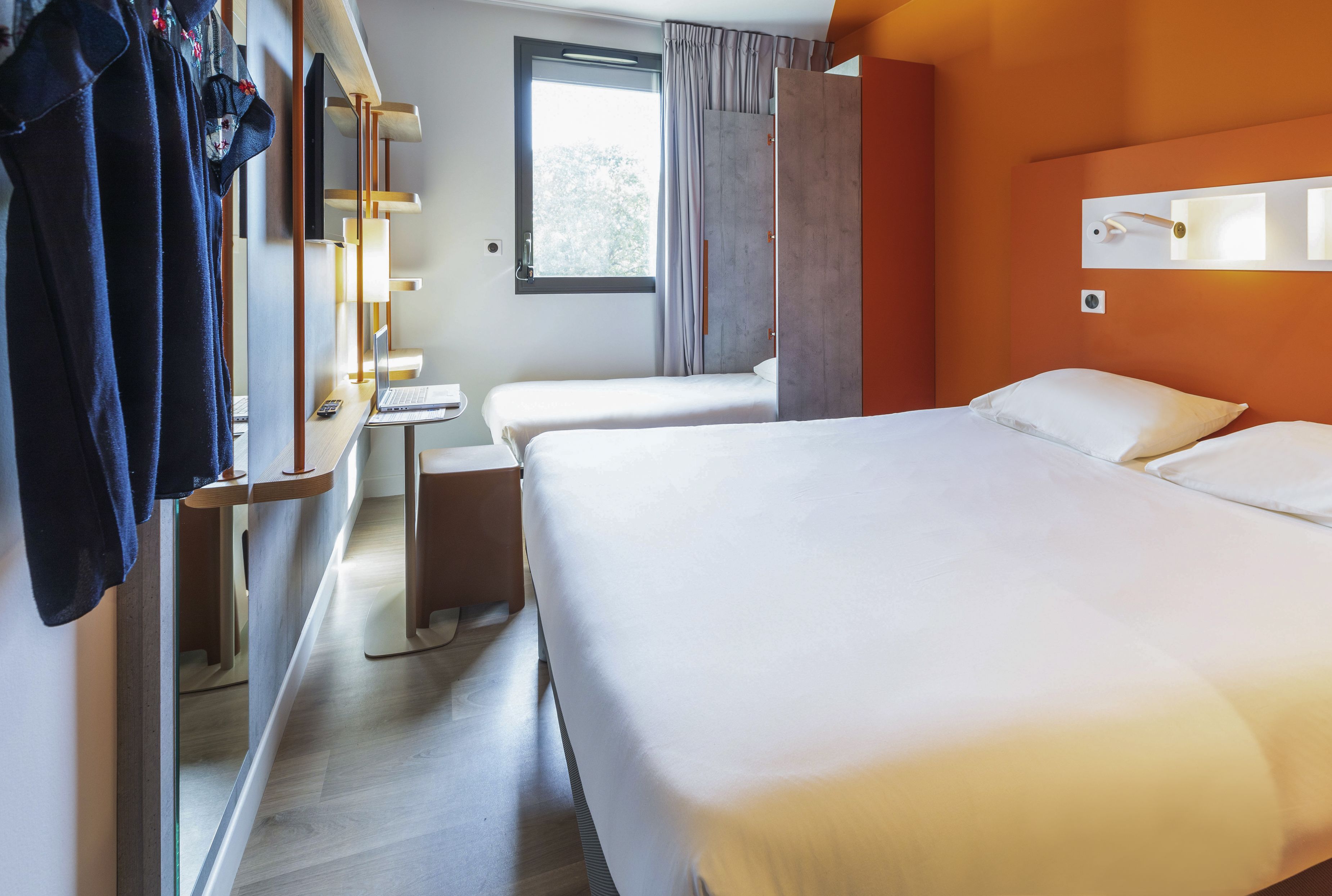 Habitación de hotel con una cama grande, un escritorio con ordenador, un espejo y una ventana con cortinas.