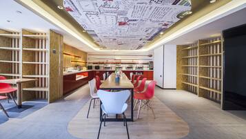 A modern dining area with a long table, red and white chairs, and a ceiling with a map design.