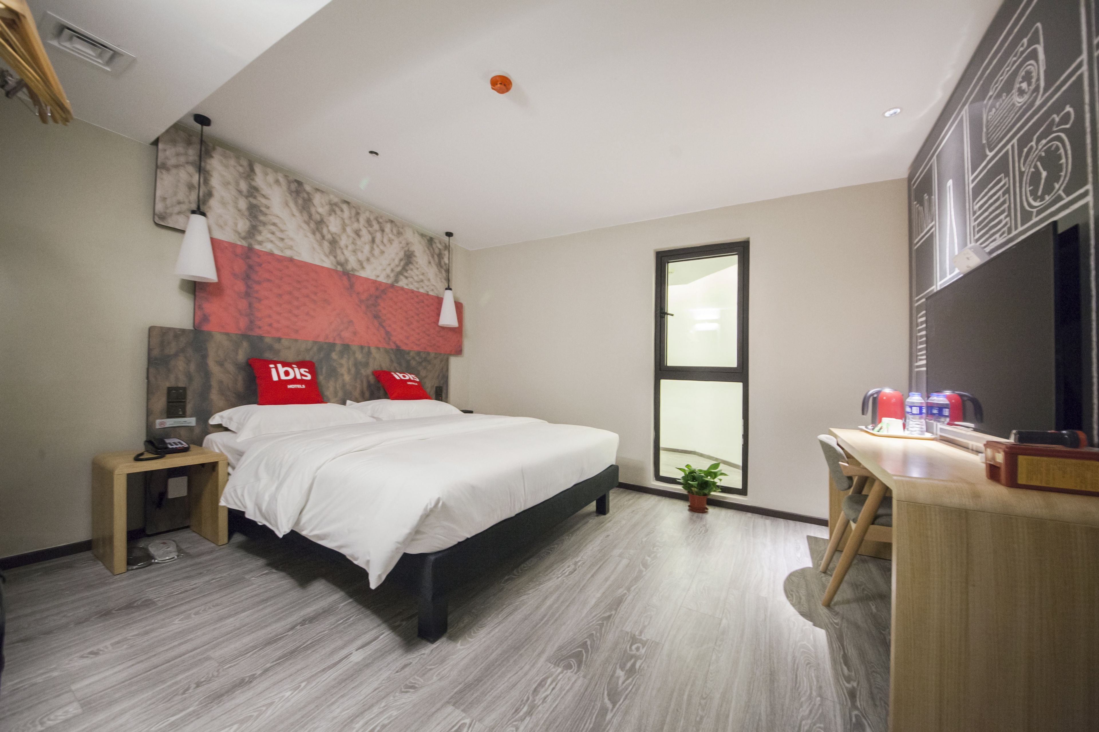 Ein modernes Hotelzimmer mit einem großen Bett, einem Schreibtisch, einem Sessel, einem kleinen Tisch, einem Telefon, einer Pflanze und einem Fenster mit Blick.