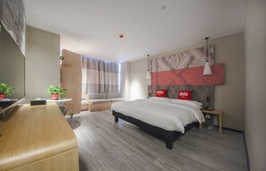 A modern hotel room with a large bed, a desk, a small table with a plant, a window with curtains, and a wall-mounted artwork. - Ibis Nantong Middle Renmin Rd Hotel (Nantong)