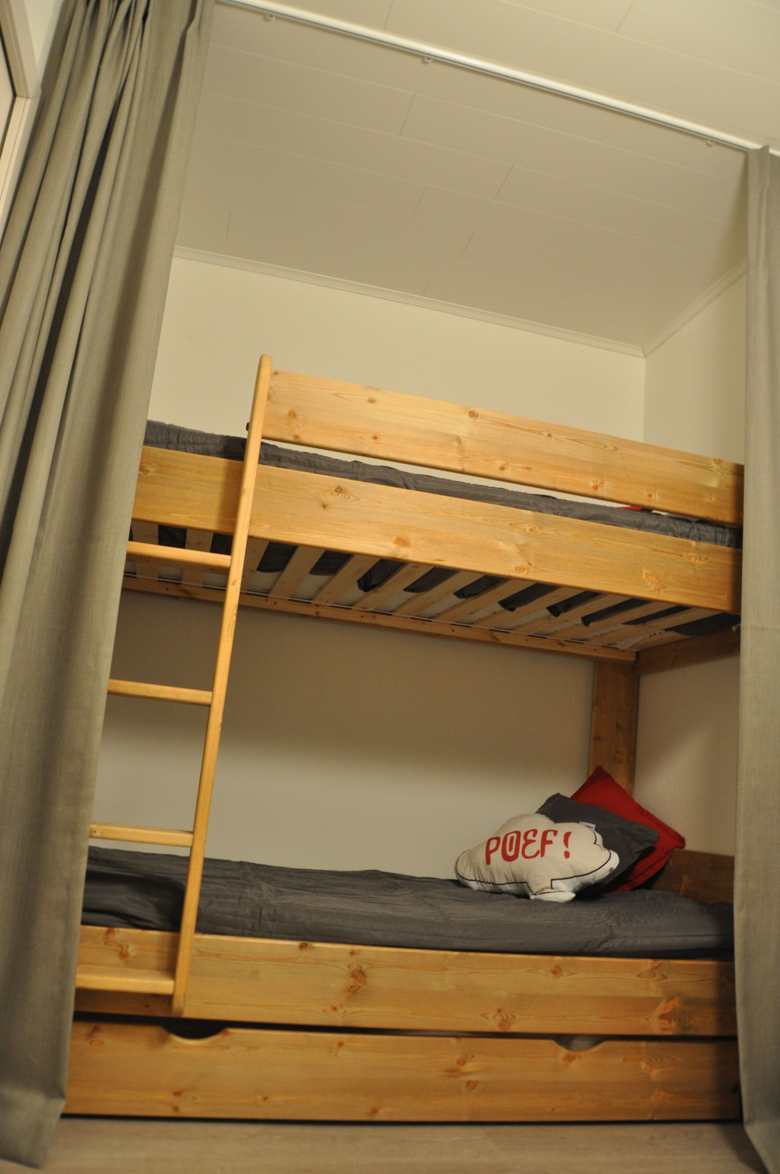 Una cama litera con escalera, un almohadón con el texto "POEF!" y un colchón gris.