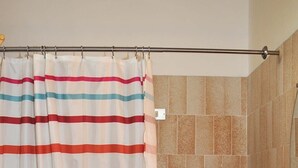 Un baño con cortina de ducha a rayas, bañera, lavamanos y paredes con azulejos.
