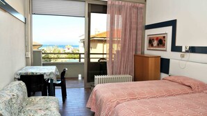 Una habitación con cama, una mesa con sillas, un radiador y vista al mar.