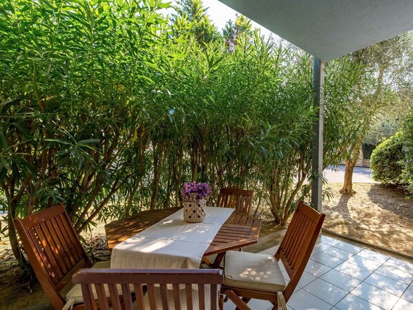 An outdoor patio with a table and chairs, surrounded by dense foliage.